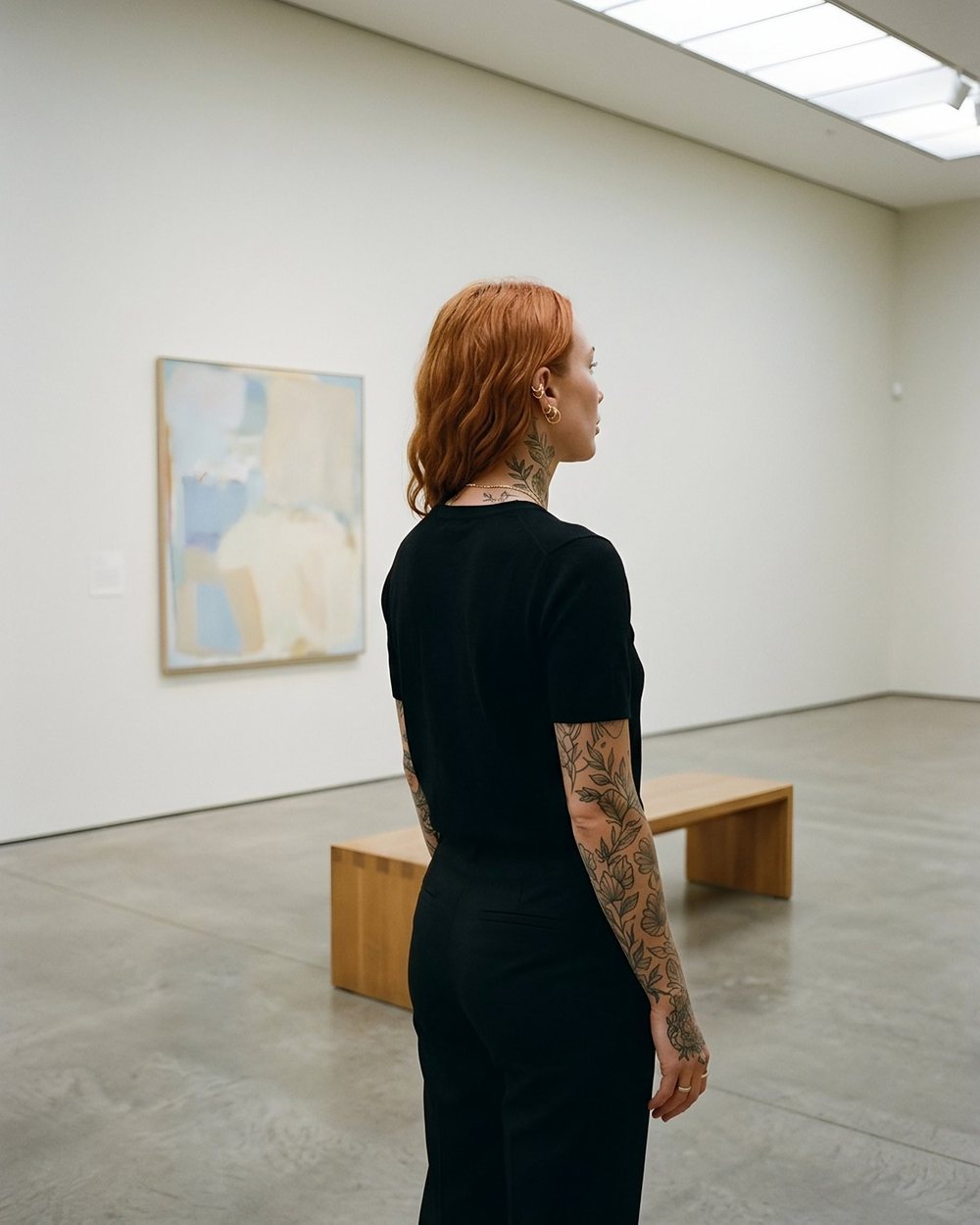 Ruby from behind in a bright, empty gallery, looking at a pale painting.